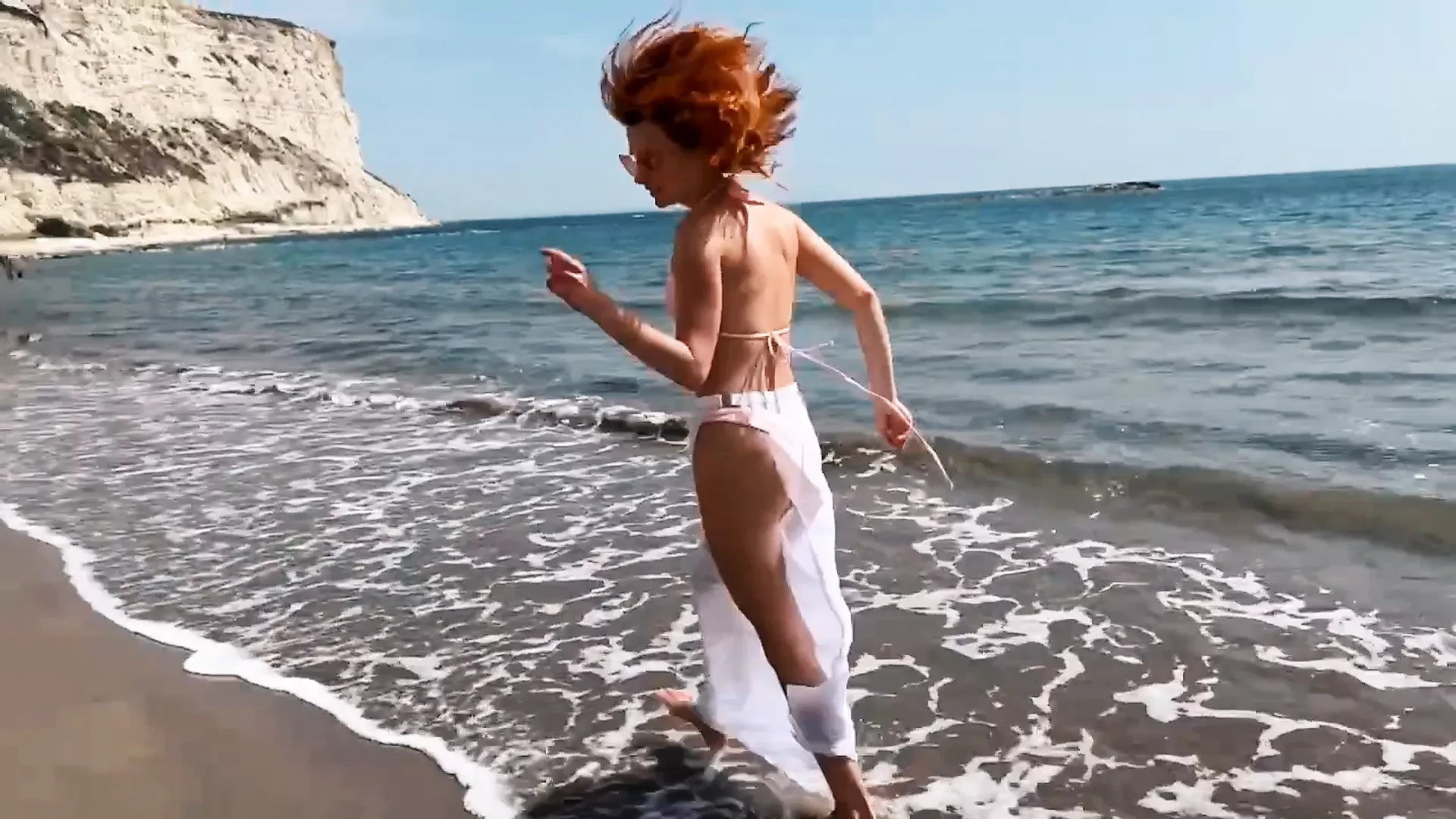 Sexy red-haired girl enjoys a walk by the sea
